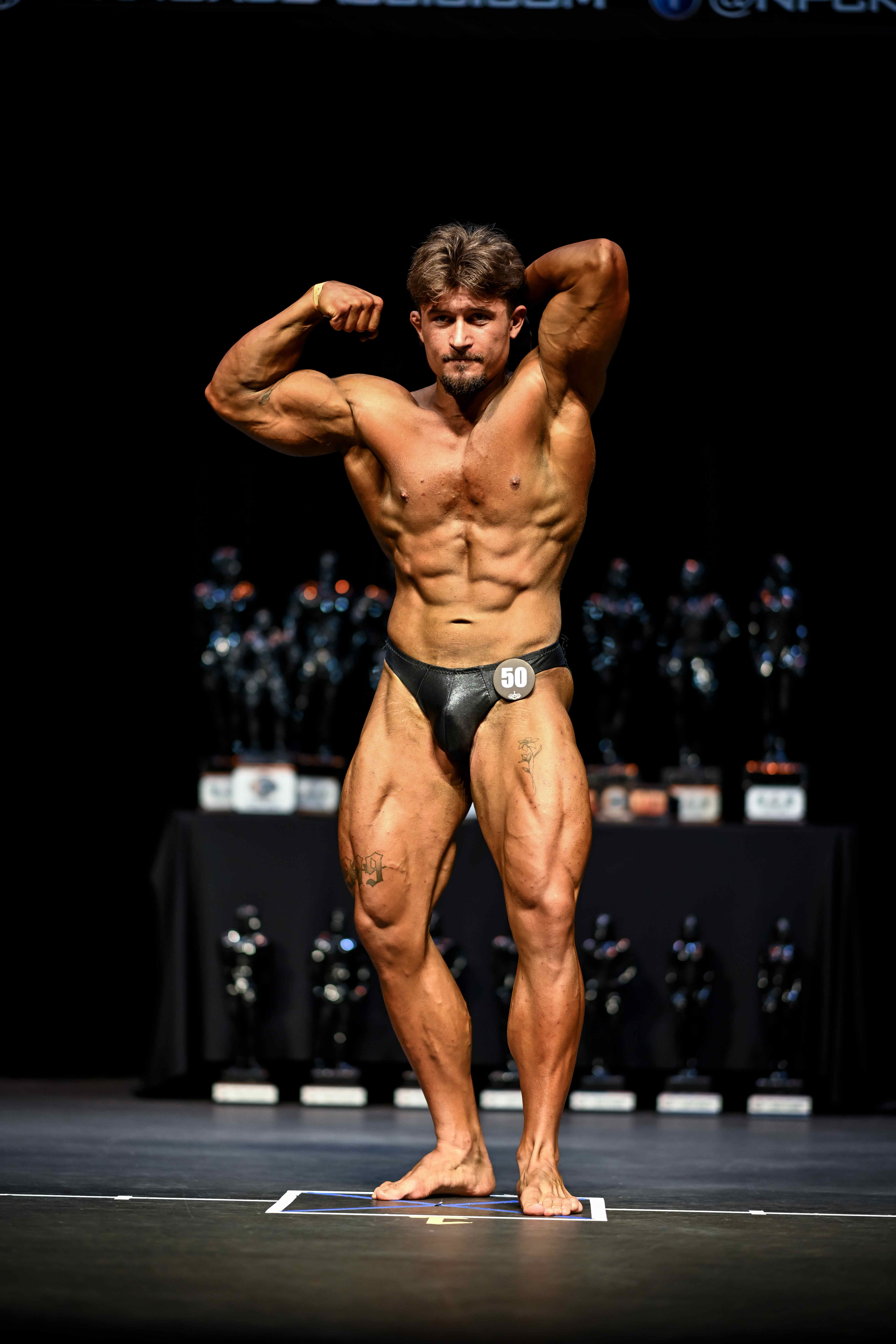 Male bodybuilder hitting a front double biceps pose on a trophy stage