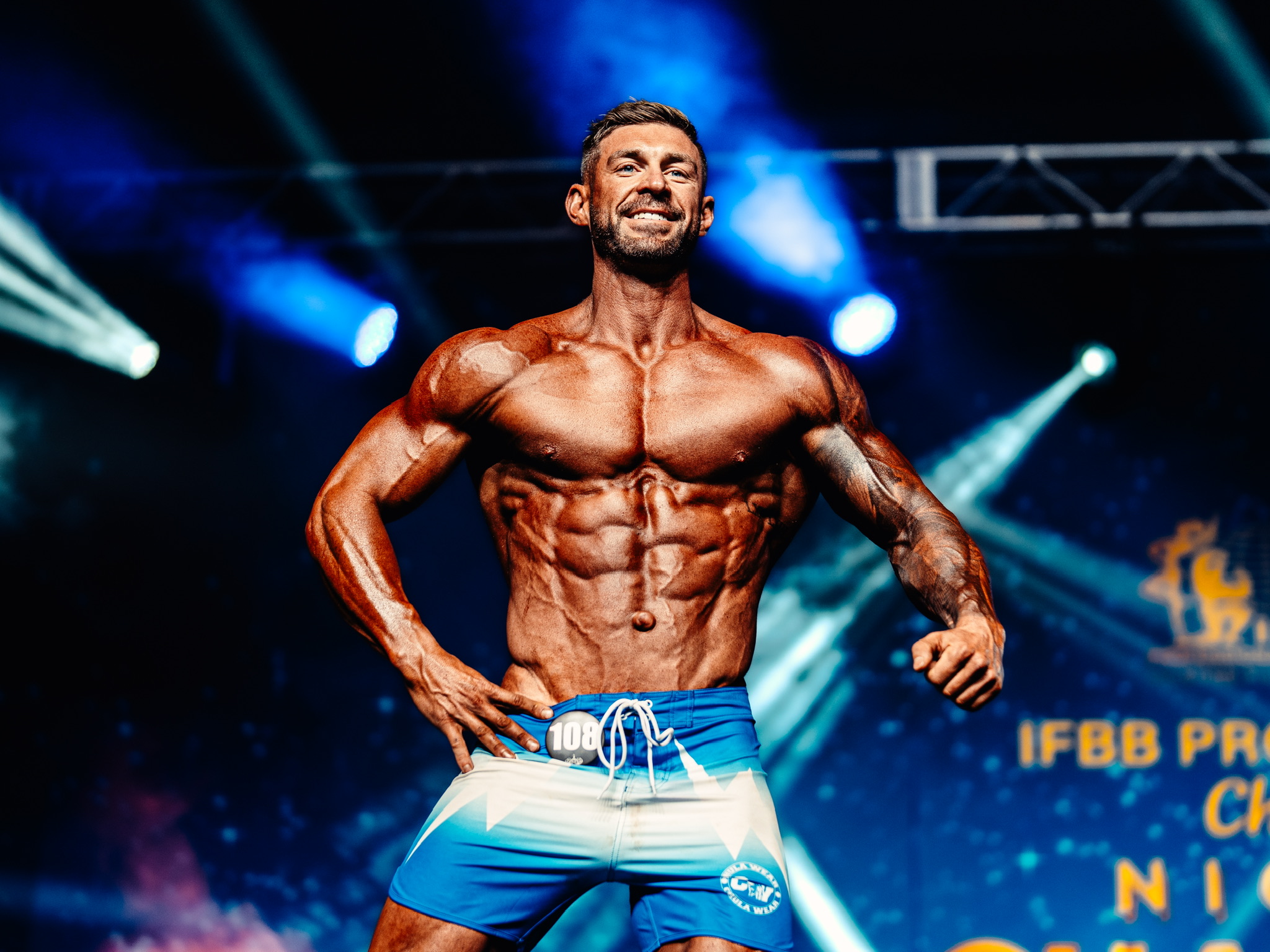 IFBB Pro physique competitor posing under blue stage lights