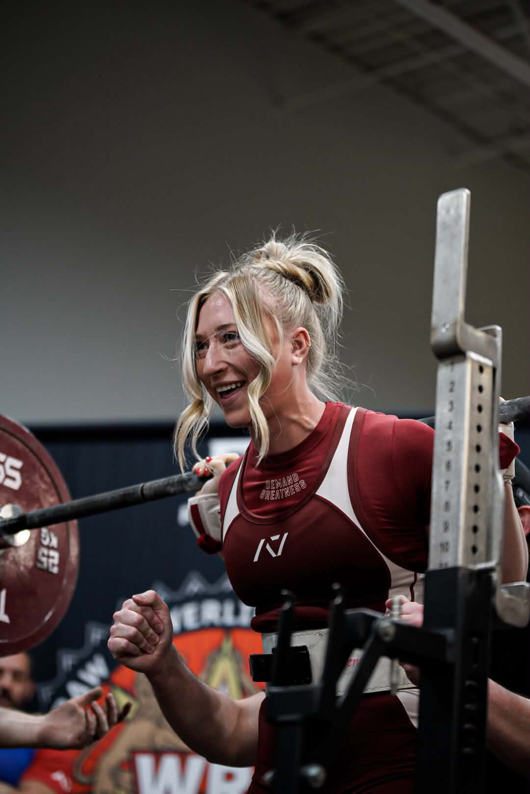 Female powerlifter smiling at the squat rack in a red singlet