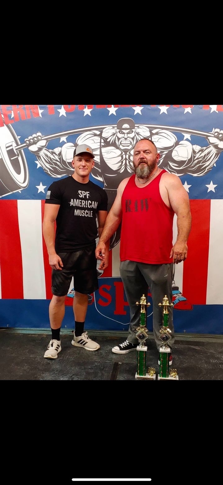 Two powerlifters holding trophies after a meet